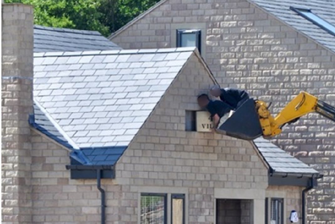 A photograph caught the moment a pair of workers stood in the bucket of a digger to fit a stone into the top of a new home in Littleborough, Greater Manchester.